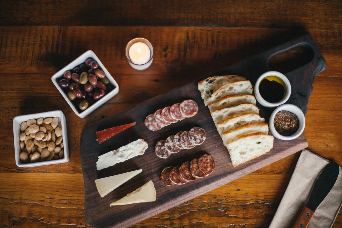 The ENSO charcuterie board: cheeses, salami, bread, olives and almonds on hand-cut black walnut, by candlelight